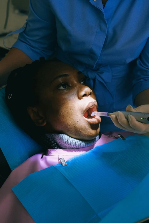 a woman is getting her teeth examined by a dentist, pexels contest winner, happening, ( ( dark skin ) ), gaping mouth, lit up, university
