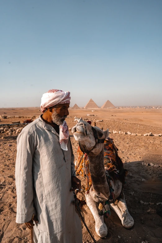 a man standing next to a camel in the desert, egyptian art, pexels contest winner, pyramids in background, city views, slide show, nat geo