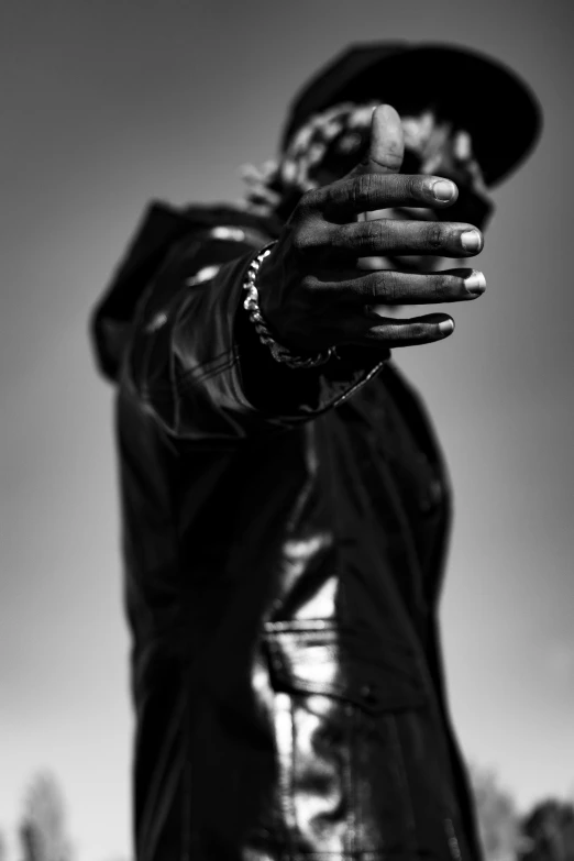 a black and white photo of a man holding a gun, young thug, wearing leather coat, emerging hands, large)}]