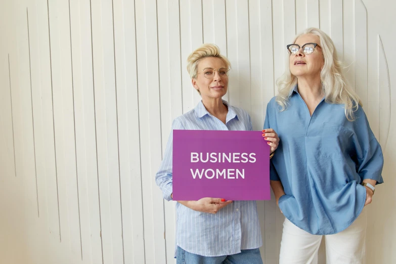 two women standing next to each other holding a sign, pixabay, business logo, white haired lady, purple, ecommerce photograph