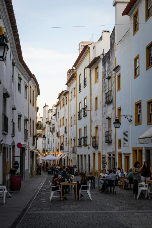 a narrow street lined with tables and chairs, brazilian ronaldo, white buildings with red roofs, golden hour, drinking