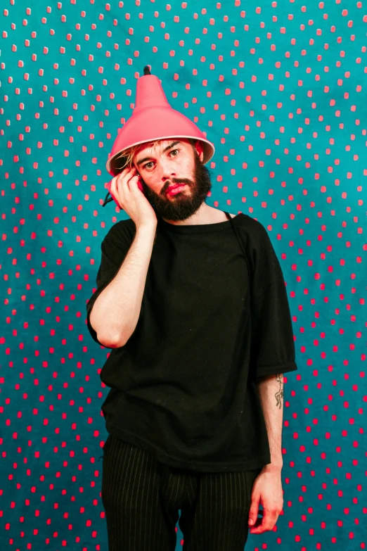 a man in a pink hat talking on a cell phone, an album cover, by Adam Dario Keel, with a beard and a black shirt, colorful backdrop, wearing pointed hoods, press photo