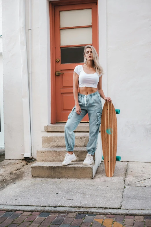 a woman standing in front of a door with a skateboard, by Robbie Trevino, trending on pexels, croptop, cargo pants, sydney sweeney, white backround