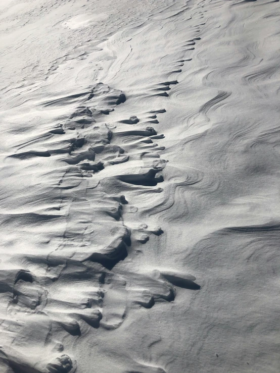 a group of footprints in the sand on a beach, an album cover, inspired by Vija Celmins, pexels contest winner, skiing, seen from a plane, high snow, intricate wrinkles