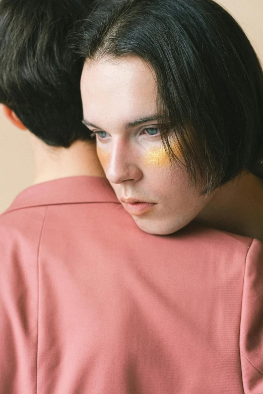 a couple of people standing next to each other, an album cover, by Attila Meszlenyi, trending on pexels, aestheticism, portrait androgynous girl, yellow makeup, looking from shoulder, iridescent skin