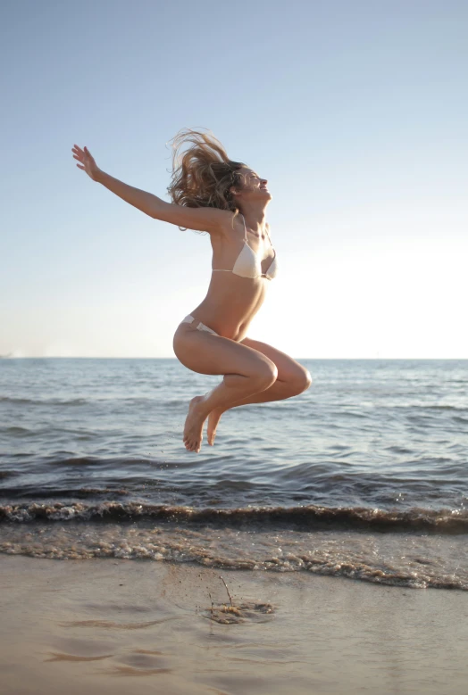 a woman jumping in the air on a beach, deep tan skin, blonde, manly, immersed