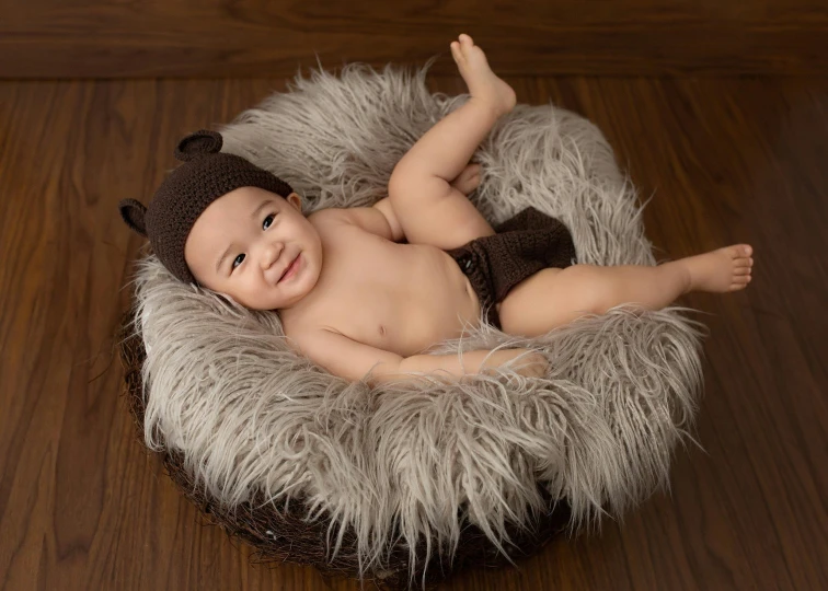 a baby laying in a basket on a wooden floor, inspired by Anne Geddes, shutterstock contest winner, grey fur, smiling, brown hat, round thighs