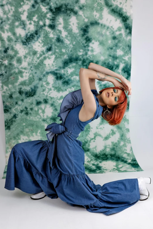 a woman in a blue dress posing for a picture, an album cover, inspired by Kaja Foglio, trending on pexels, at a fashion shoot, swirling fabric, overalls, backdrop