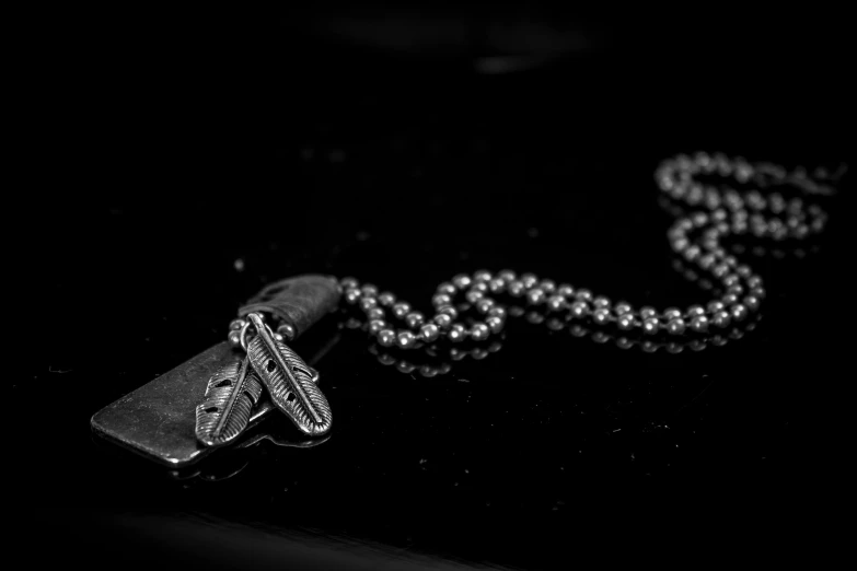 a black and white photo of a dog tag on a chain, a black and white photo, unsplash, dagger, leather jewelry, bead necklace, platinum jewellery