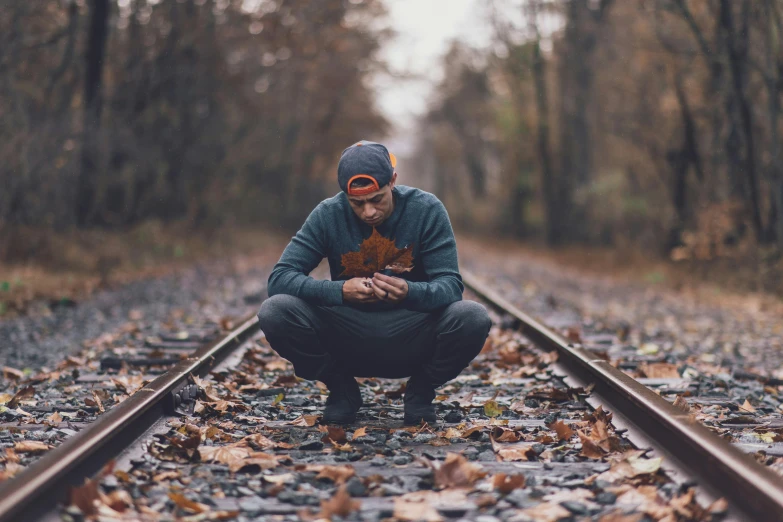 a man squatting down on a train track, pexels contest winner, covered in fallen leaves, deep in thought, without text, lovecratian