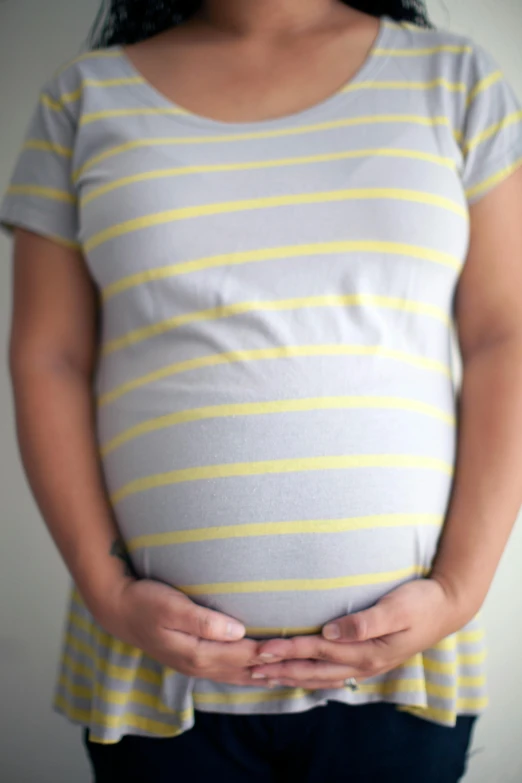 a pregnant woman holding her belly in her hands, pexels, silver and yellow color scheme, wearing stripe shirt, realistic », 2029