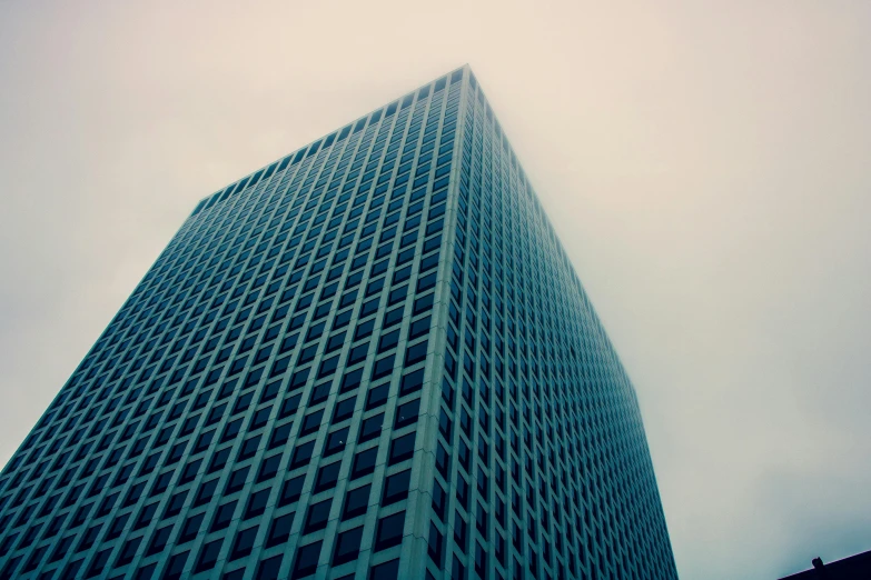 a tall building sitting in the middle of a city, an album cover, unsplash, brutalism, cyan mist, office building, square lines, big overcast