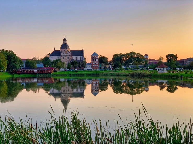 a large building sitting on top of a lush green field, by Jan Tengnagel, pexels contest winner, water reflections, sunset panorama, beautiful small town, church in the background