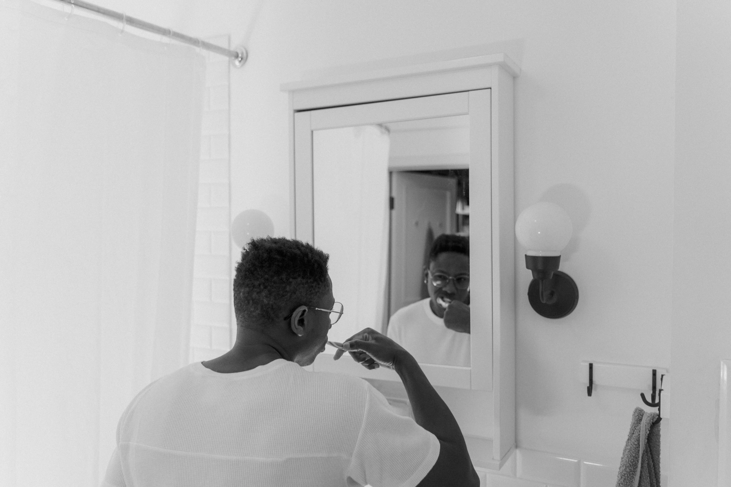 a man brushing his teeth in front of a mirror, inspired by Carrie Mae Weems, pexels contest winner, minimalism, low quality photo, wearing square glasses, black on white, maintenance