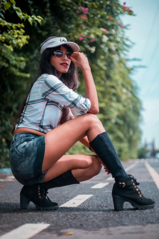 a woman sitting on the side of the road, by Max Dauthendey, pexels contest winner, realism, hot-pants, doing a sassy pose, trending on artstion, wearing sunglasses and a cap