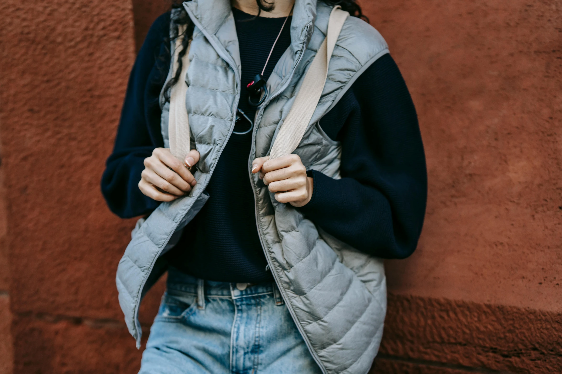 a woman standing in front of a red wall, by Nina Hamnett, trending on pexels, grey hoodie, technical vest, wearing a waistcoat, student