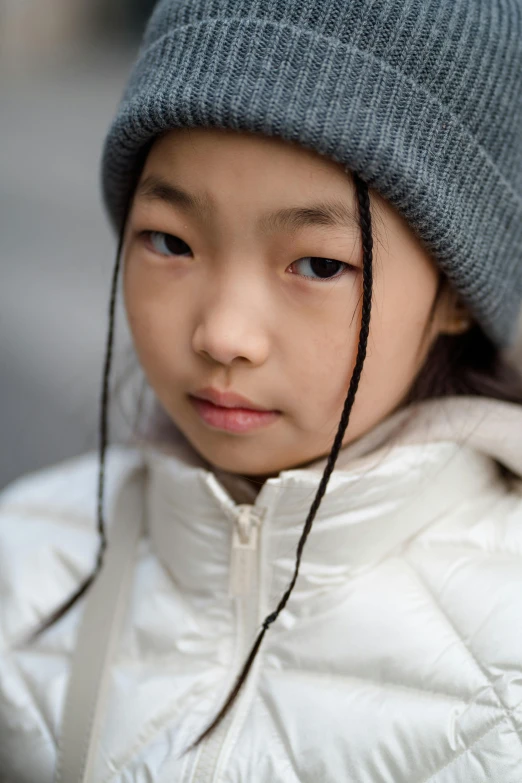 a close up of a child wearing a hat, inspired by Nara Yoshitomo, trending on unsplash, model wears a puffer jacket, looking serious, humans of new york, girl with plaits