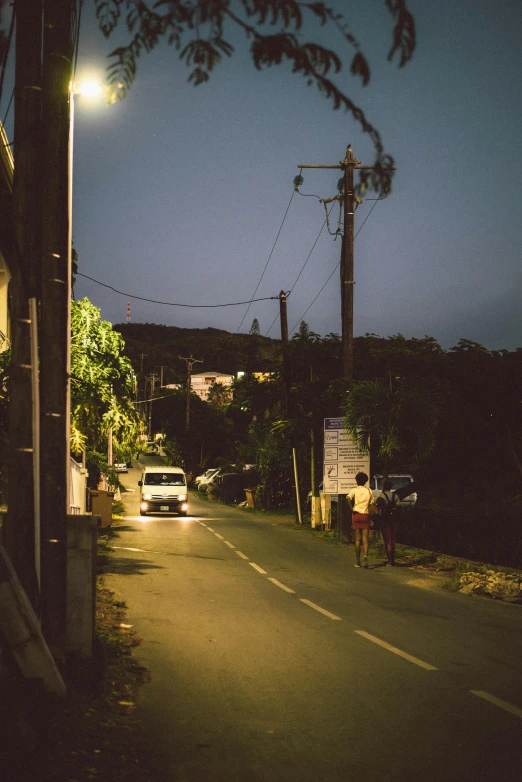 a car driving down a street at night, a picture, inspired by Nan Goldin, unsplash, happening, okinawa japan, on a village, late afternoon lighting, hills