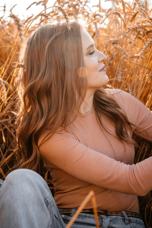 a woman sitting in a field of tall grass, light brown long wavy hair, at sunset in autumn, profile image, photoshoot for skincare brand