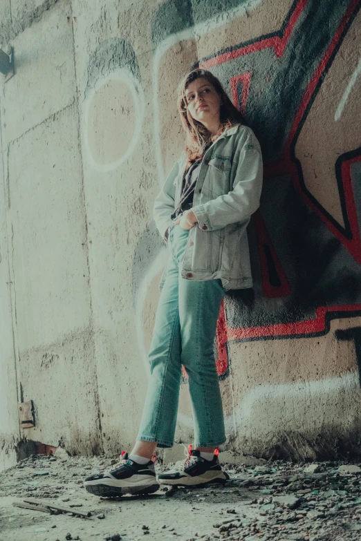 a woman standing in front of a graffiti covered wall, a colorized photo, inspired by Elsa Bleda, trending on pexels, green corduroy pants, ((greenish blue tones)), concert, sunfaded