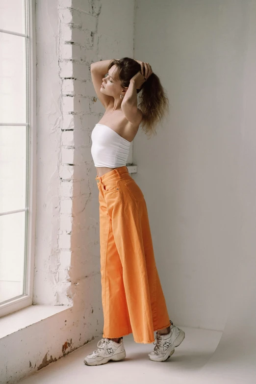 a woman standing in front of a window, trending on pexels, large pants, white and orange, anna nikonova aka newmilky, croptop