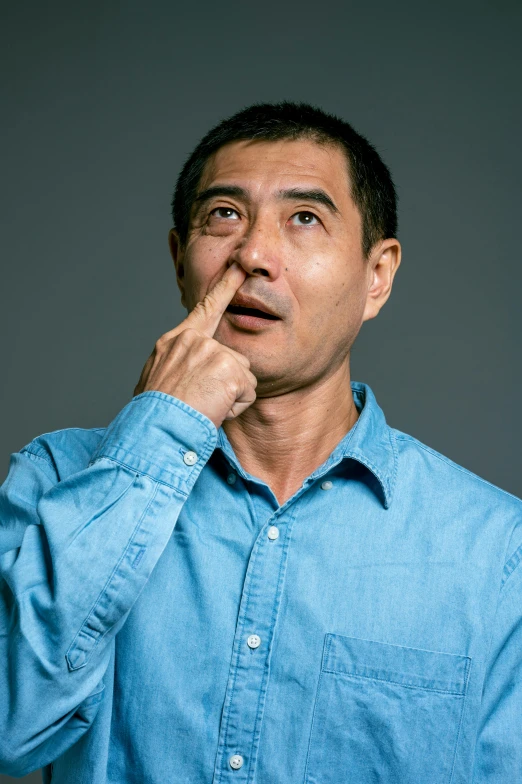 a man in a blue shirt holding his finger to his mouth, by Yan Liben, crooked nose, plain background, gregg araki, pondering