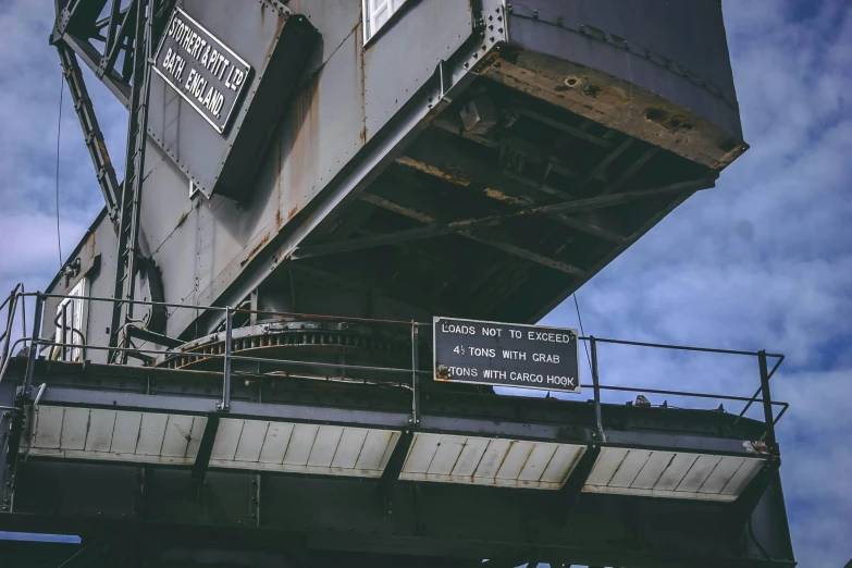 a train traveling over a bridge under a cloudy sky, a photo, unsplash, graffiti, old signs, aircraft carrier, worksafe. instagram photo, sitting in a crane