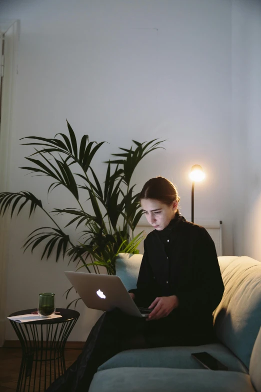 a woman sitting on a couch using a laptop, inspired by Elsa Bleda, unsplash, small and cosy student bedroom, portrait of sanna marin, low lighting, slightly minimal