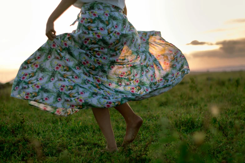 a woman standing on top of a lush green field, by Alice Mason, unsplash, renaissance, wide skirts, floral patterned skin, in motion, evening sun