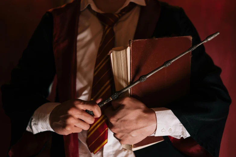 a man in a suit holding a book and a wand, trending on pexels, renaissance, hogwarts gryffindor common room, tech robes, fancy dress, dirty harry potter