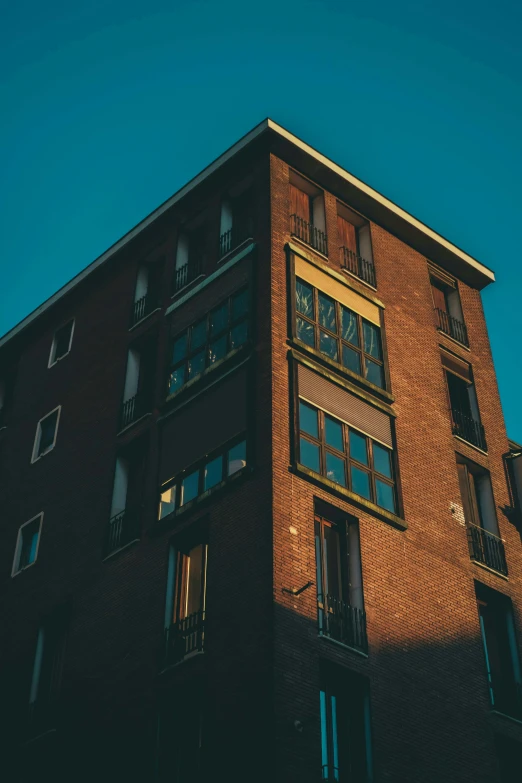 a tall brick building with lots of windows, inspired by Elsa Bleda, pexels contest winner, modernism, brown, neighborhood, low light, blue sky