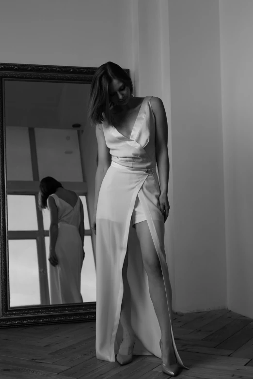a woman in a white dress standing in front of a mirror, a black and white photo, inspired by Gabriel Ba, tumblr, jumpsuit, silk dress, evening, thirst