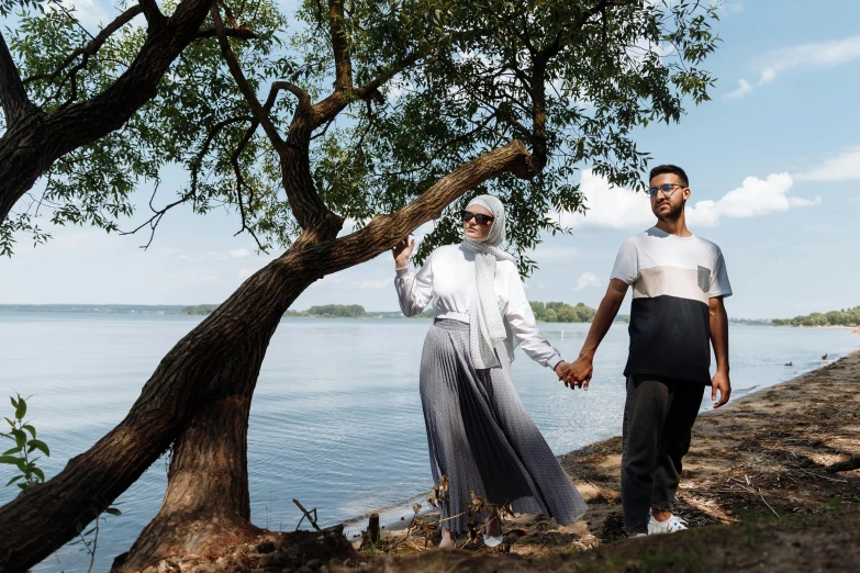 a man and a woman holding hands by the water, a portrait, by Basuki Abdullah, unsplash, hurufiyya, with a tall tree, on a sunny day, diverse outfits, muslim