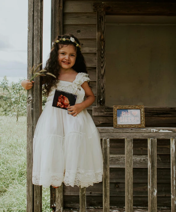 a little girl in a white dress holding a book, an album cover, by Lucia Peka, pexels contest winner, polaroid picture, little bo peep, epk, dressed in a beautiful