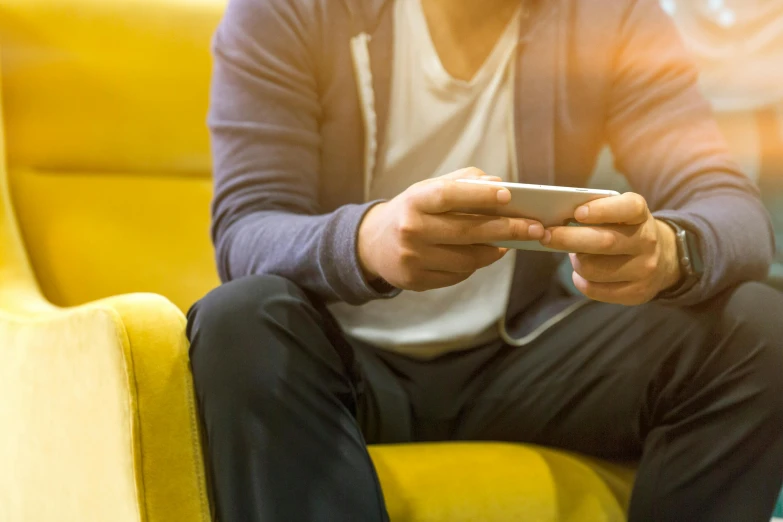 a man sitting on a yellow couch holding a cell phone, shutterstock, renaissance, video game icon, blurred photo, indie games, real trending on instagram image