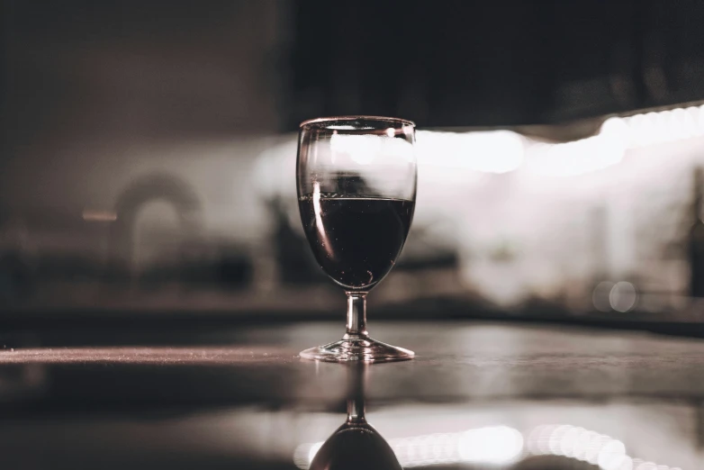 a glass of wine sitting on top of a counter, unsplash, medium format. soft light, almost black, the sacred cup of understading, full of reflections