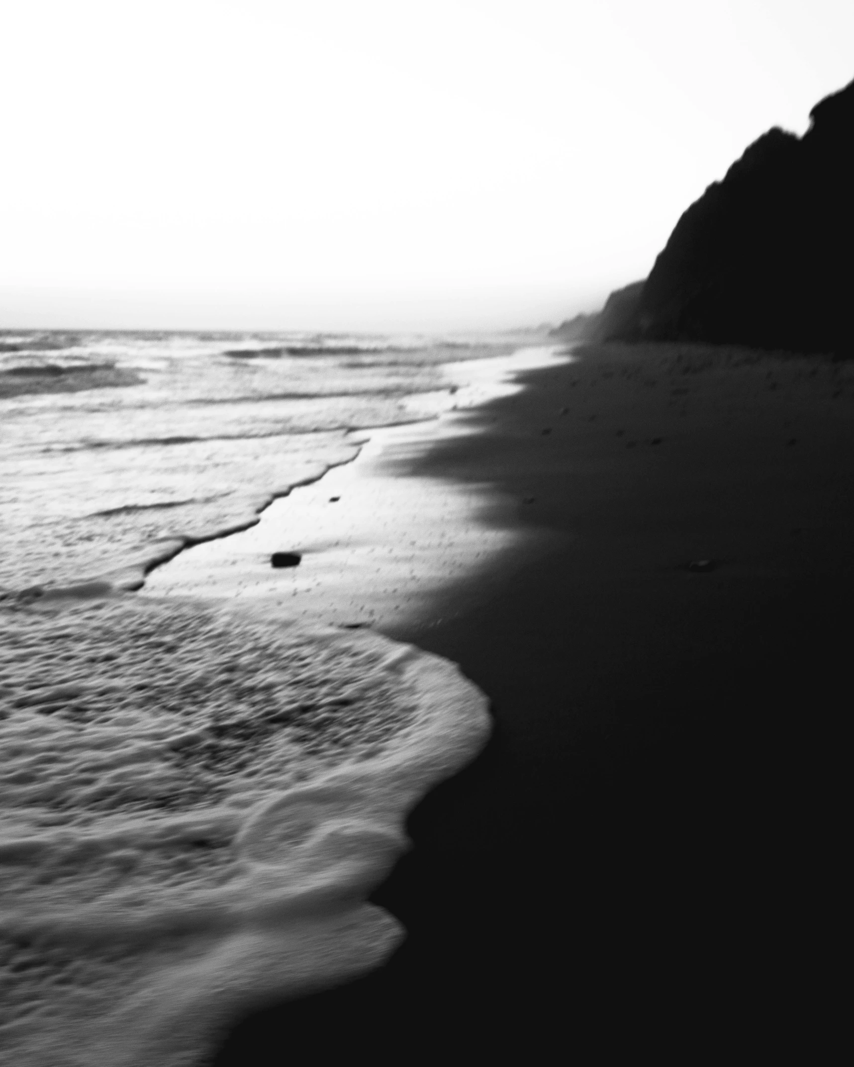 a black and white photo of a beach, a black and white photo, inspired by Max Dupain, unsplash, maybe small waves, cliff side at dusk, santa monica beach, :: morning