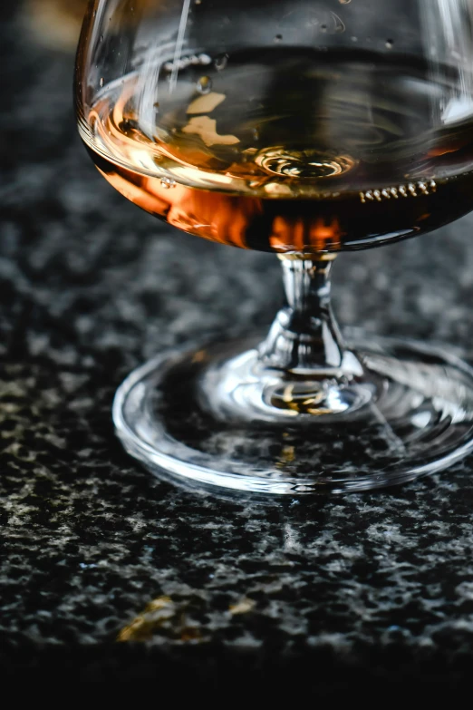 a close up of a glass of wine on a table, inspired by Richmond Barthé, renaissance, rum, on a dark rock background, zoomed in, polished