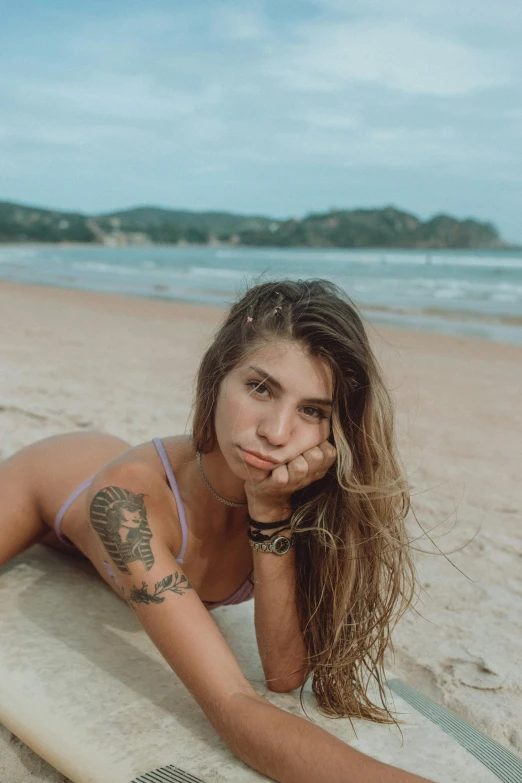 a woman laying on top of a surfboard on a beach, a tattoo, inspired by Elsa Bleda, pexels contest winner, renaissance, looking directly at the camera, brazil, headshot profile picture, slightly tanned