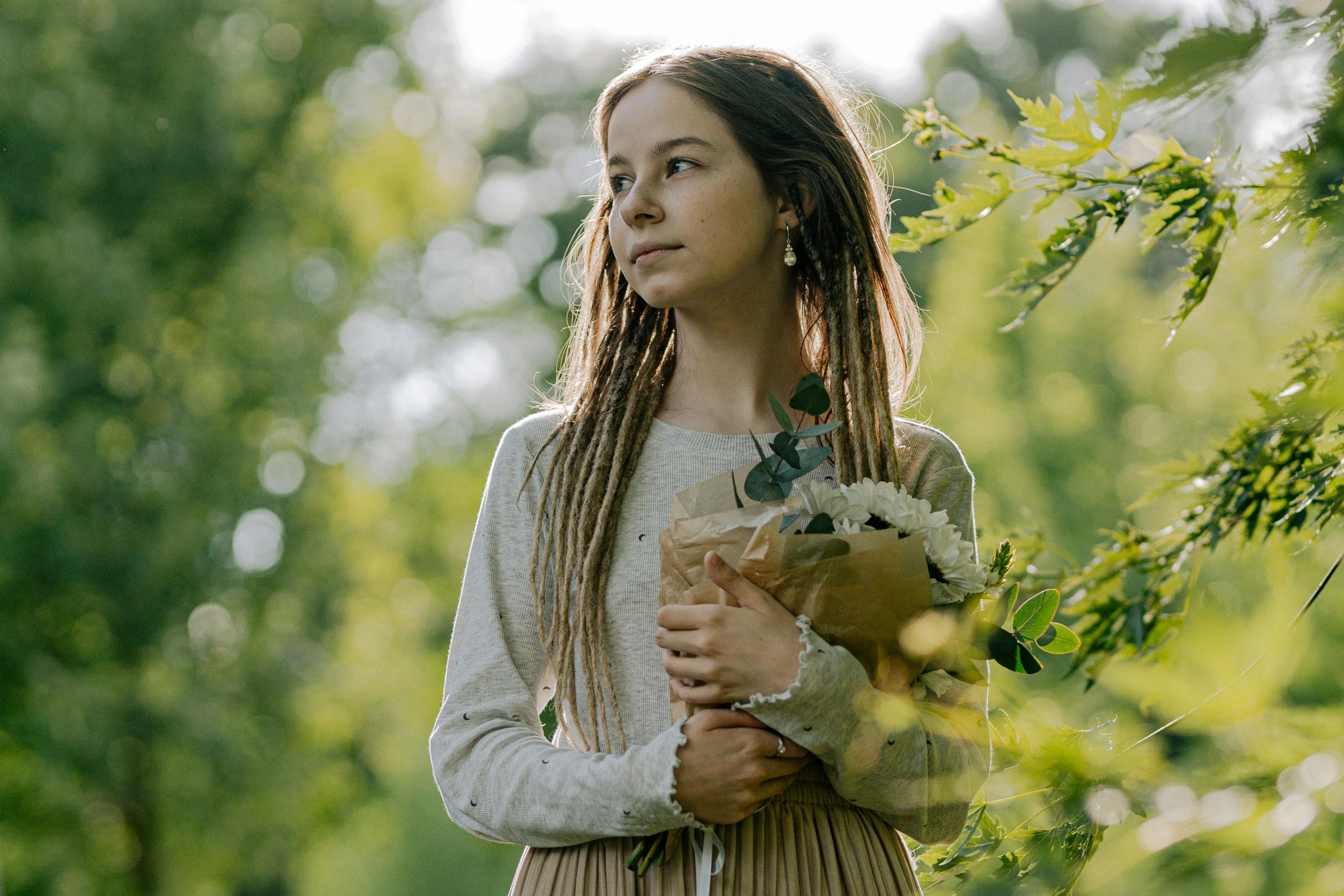 a young girl holding a bunch of flowers, by Emma Andijewska, shutterstock, renaissance, dafne keen, against the backdrop of trees, cinematic morning light, avatar image