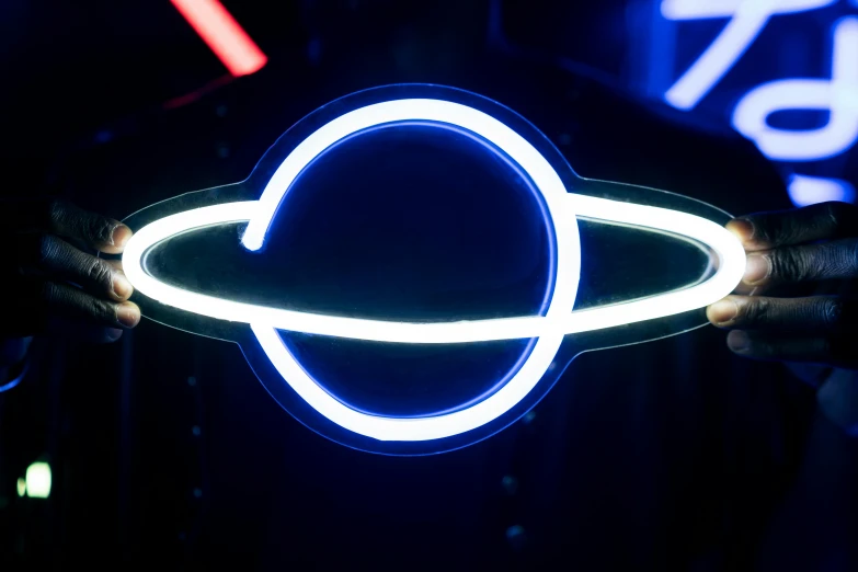 a person holding a neon ring in front of a neon sign, by Doug Ohlson, unsplash, kinetic art, planet saturn, avatar image, neon blue, vintage space station logo