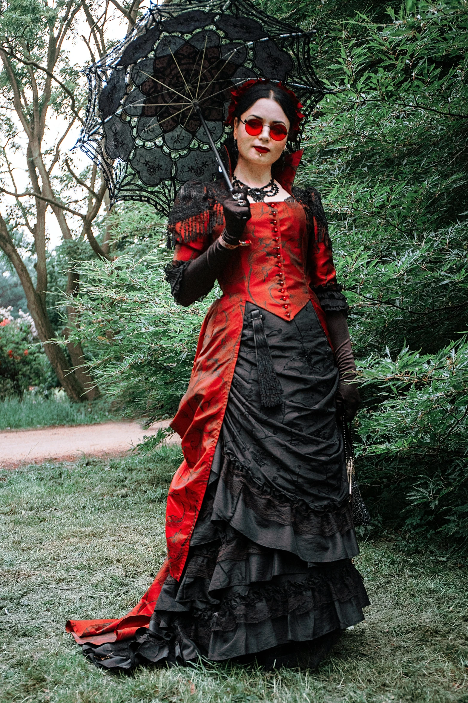 a woman in a red and black dress holding an umbrella, inspired by Louis Grell, pexels contest winner, gothic art, wearing victorian brass goggles, standing in a botanical garden, elaborate costume, slide show