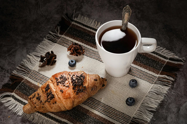 a croissant sitting on top of a table next to a cup of coffee, pexels contest winner, black and brown colors, linen, thumbnail, listing image