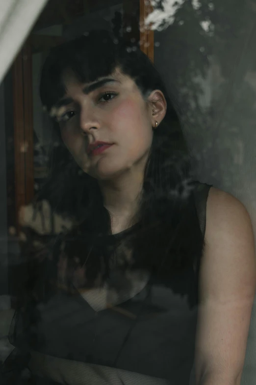 a woman is looking out of a window, inspired by Elsa Bleda, she has black hair with bangs, on a gray background, broken mirror, promo image