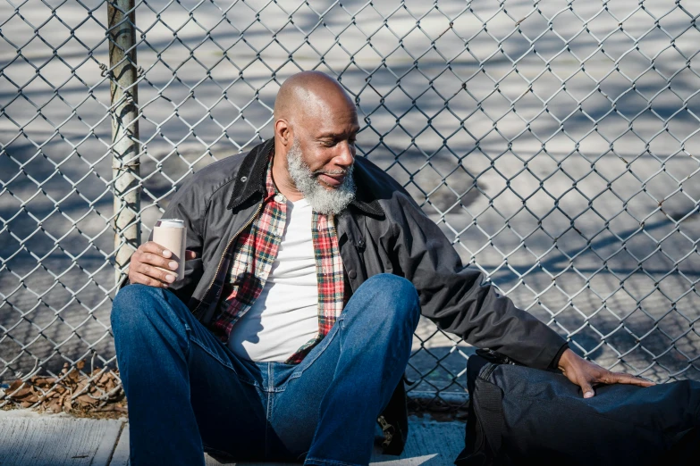 a man sitting on the ground next to a fence, by Washington Allston, pexels contest winner, happening, bald head and white beard, lebron james solemn at tea party, homeless, mike tyson