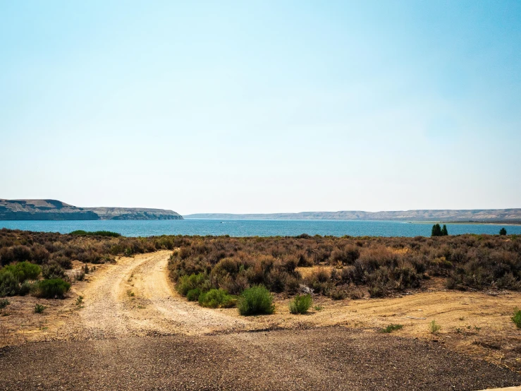 a dirt road next to a body of water, unsplash, land art, oregon trail, clear skies in the distance, instagram photo, listing image