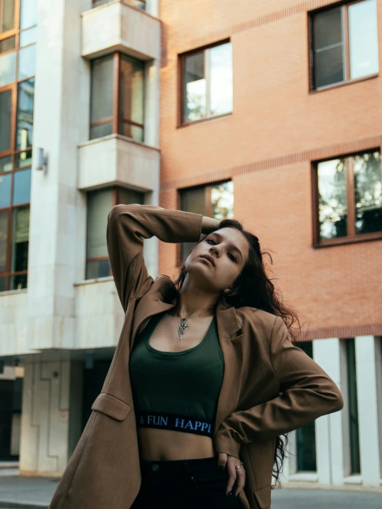 a woman standing in front of a tall building, inspired by Elsa Bleda, trending on unsplash, renaissance, wearing a worn out brown suit, bralette, wearing green jacket, satisfied pose