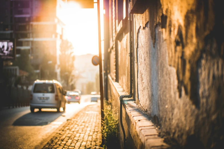 a car driving down a street next to a building, by Kristian Zahrtmann, pexels contest winner, sunlight glistening, waiting behind a wall, dirty streets, small depth of field