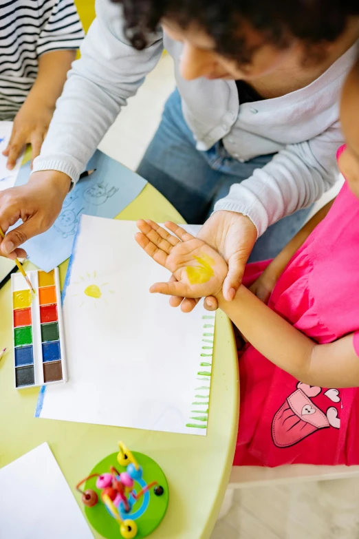 a group of children sitting around a table, a child's drawing, inspired by Helen Frankenthaler, pexels, lady using yellow dress, painting on a badge, educational supplies, a high angle shot