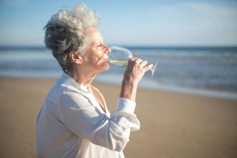 a woman drinking a glass of wine on the beach, by Julian Allen, pexels contest winner, silver haired, enjoying the wind, photograph of april, bubbly